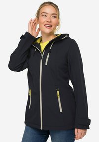 Veste softshell marine avec capuche, accents beiges, fermeture éclair à l'avant et poches latérales. Elle possède des poignets ajustables et une capuche avec cordon de serrage.