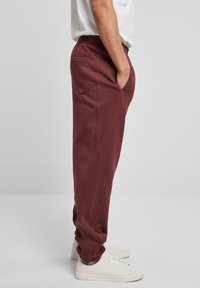 Pantaloni de training bordeaux, cu o croială lejeră, talie elastică, buzunare laterale și manșete conice, asociați cu adidași albi. Material moale, design minimalist.