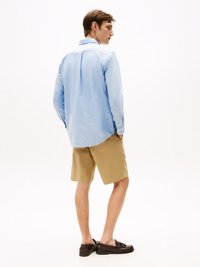 Lichtblauw overhemd met lange mouwen en een rugplooien, gecombineerd met tan shorts en donkerbruine boot schoenen. Soepele stof, casual pasvorm.