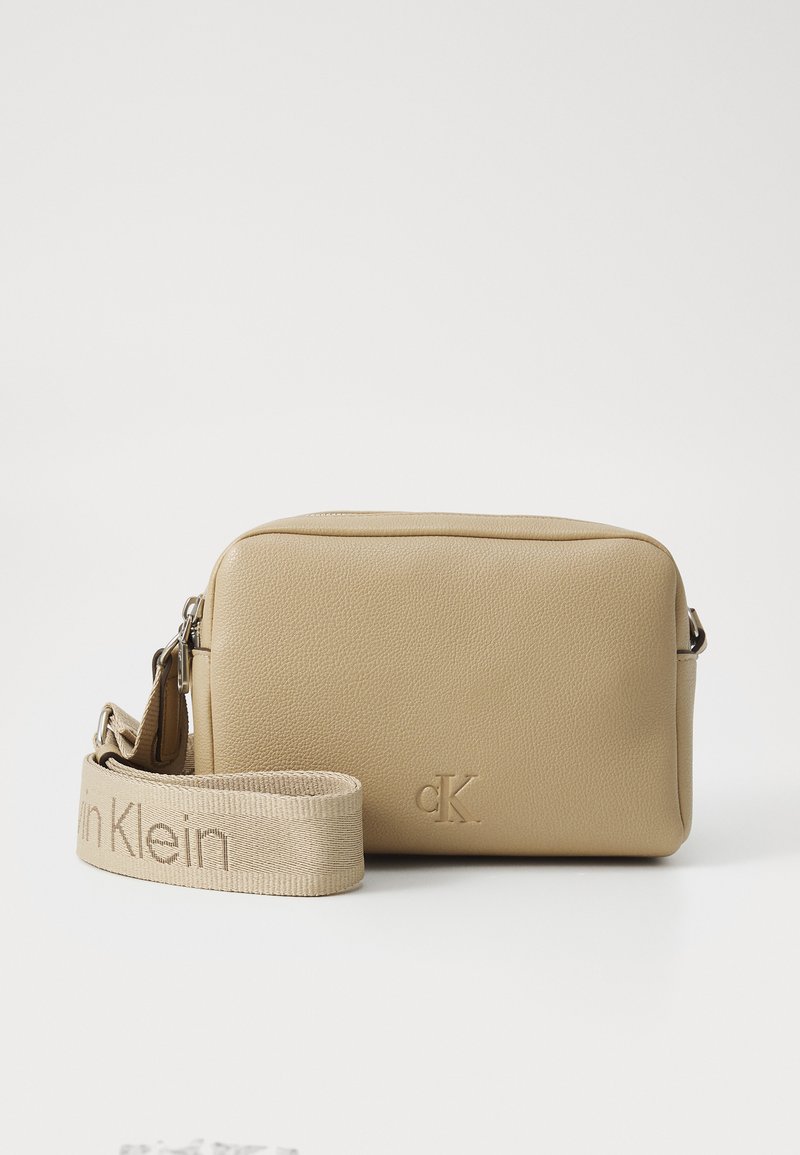 Tan lærcrossbody-veske med teksturert overflate, glidelås og justerbar stropp med "calvin Klein"-merke.