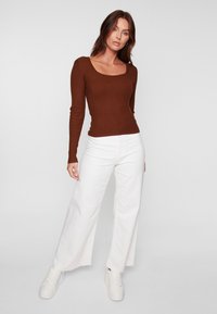 Haut long à manches en maille côtelée marron avec un décolleté carré, associé à un pantalon large blanc et des baskets crème, présentant des bords effilochés à l'ourlet.
