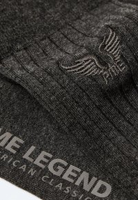 Ciemnoszara dzianina ma subtelnie żebrowaną teksturę, z haftowanym wzorem skrzydła oraz napisem "FAME LEGEND AMERICAN CLASSICS."