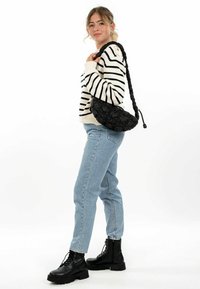 Borsa a spalla nera trapuntata con tracolla intrecciata, abbinata a un maglione bianco a righe e jeans azzurri chiari, indossata con stivali neri stringati.