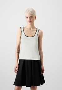 Lys grønn tank topp med svart zigzag-trim, kombinert med et svart utsvikt skjørt. Toppen har en rund hals og en tettsittende design.