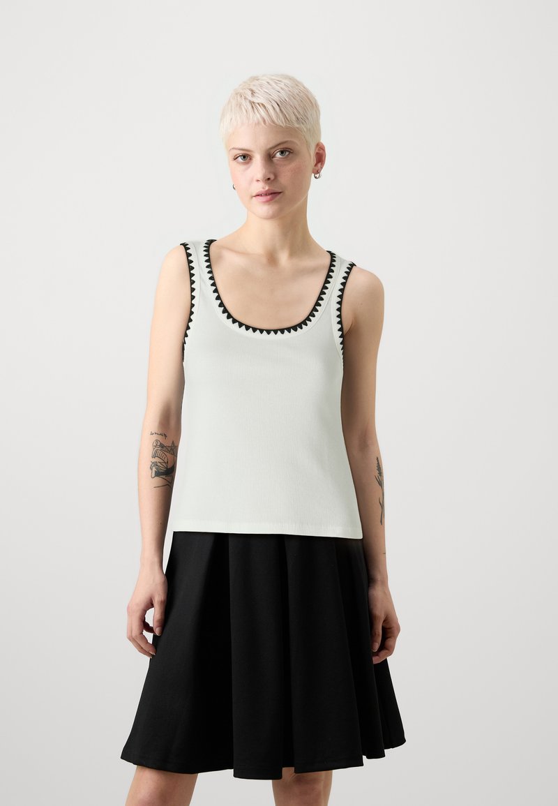 Lys grønn tank topp med svart zigzag-trim, kombinert med et svart utsvikt skjørt. Toppen har en rund hals og en tettsittende design.