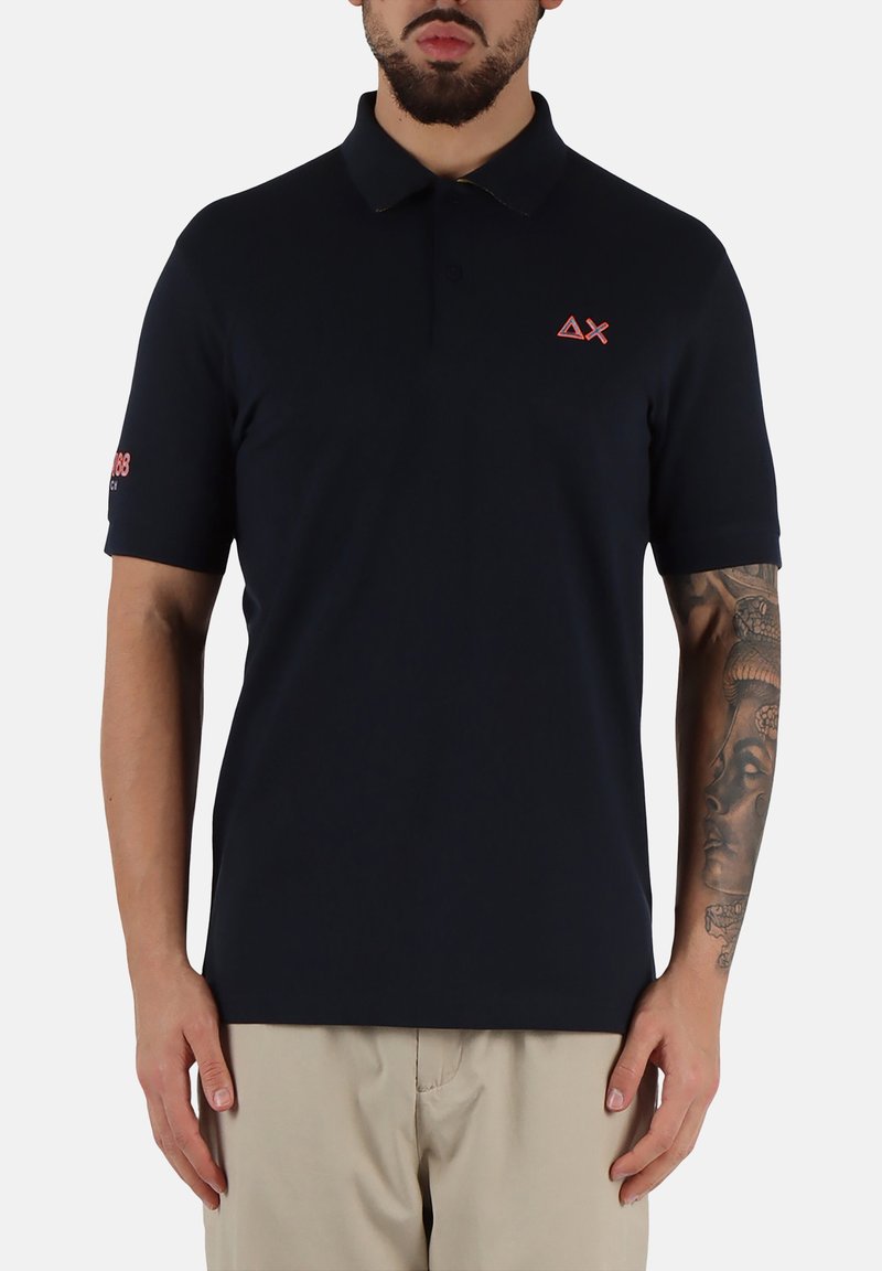 Polo shirt blu navy realizzato in un tessuto liscio, dotato di colletto, maniche corte e piccolo logo rosa sul petto e sulla manica.