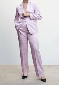 Pink satin suit with a subtle dot pattern; fitted blazer with peak lapels and wide-leg trousers; paired with sleek black heels.