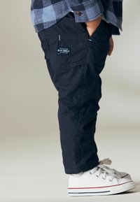 Marineblå cargo bukser med flere lommer og stikning, parret med hvide sneakers med røde og blå accenter.