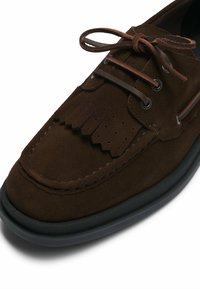 Braune Wildlederschuhe mit einem Fransen-Design, abgerundeter Zehenpartie und schwarzer Gummisohle. Ausgestattet mit braunen Schnürsenkeln und Metallösen für sicheren Halt.