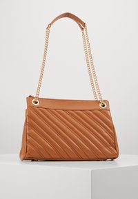 Vaaleanruskea päällystetty käsilaukku, jossa on kultaketjuhihnat, suorakaiteen muotoinen, sileä pinta ja vinosti tikatut yksityiskohdat. Vetoketjukiinnitys ylhäällä.