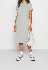 Vaaleanharmaa puuvillamekko, jossa on lyhyet hihat ja suora leikkaus, yhdistettynä valkoisiin tennareihin ja pieneen valkoiseen krokopintaisiin käsilaukkuun.