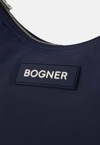 Temno modra torba z gladko najlonsko teksturo, srebrnim zadrgo in izstopajočim belim logotipom "BOGNER" na pravokotnem plaketu.