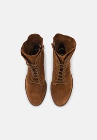 Bottes de cheville en daim marron avec un bout arrondi, lacets à l'avant et garnitures décoratives sur le côté. Texture lisse et tige de hauteur moyenne.