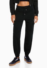 Pantaloni cargo neri con vita e polsini elasticizzati, dotati di tasche laterali e una vestibilità comoda, abbinati a sneakers nere.