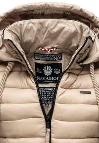 Beige pufferjakke med hætte, med kontrastfarvede snore, lynlåslukning og mærkater på det indvendige foer. Tekstureret overflade.