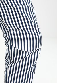 Marinblå och vitrandig tyg visar en åtsittande design med synlig sömnad och en ficka på knäet för extra detalj.