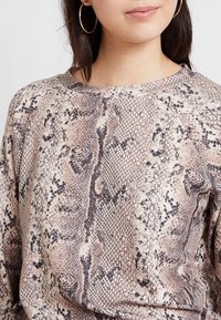 Długi rękaw top z beżowym i brązowym wzorem skóry węża, wykonany z miękkiego materiału o teksturowanym wykończeniu i okrągłym dekoltem.