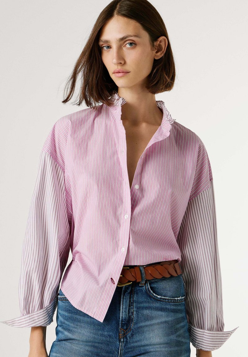 Nööbitav särk, millel on roosa- ja valgekirjud triibud, õhuke kangas, volangikaelus ja pikad varrukad. Sobitatud siniste teksade ja pruuni vööga.