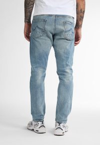 Jeans de mezclilla azul deslavados con un corte ajustado, que cuentan con dos bolsillos traseros y detalles de costura sutiles. Llevados con zapatillas deportivas blancas.
