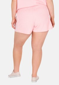 Rosa bomullsshorts med ett strukturerat ribbat mönster, med elastisk midja och lös passform, som slutar vid mitten av låret. Skorna är ljusgrå sneakers.
