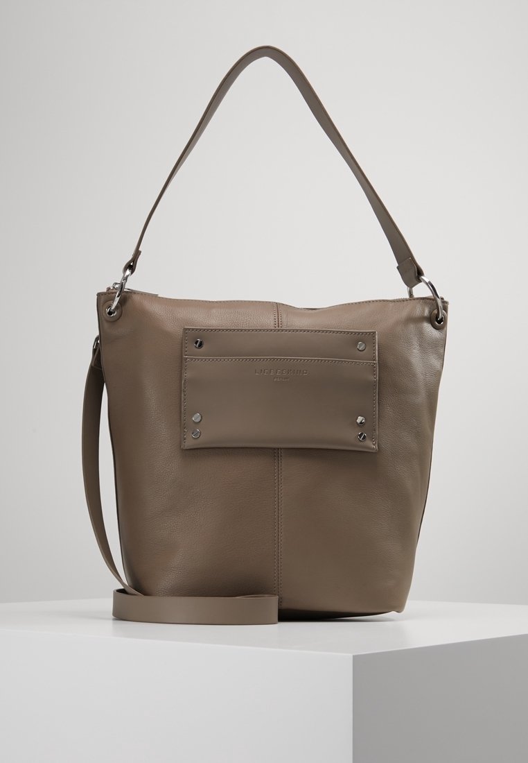 Läderhandväska i taupe med en platt framficka, silverfärgade detaljer, en bred rem och en strukturerad men mjuk textur.