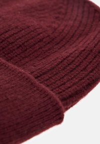 Gorro de punto burdeos con textura acanalada; material de lana suave y detalle de borde plegado. La vista en primer plano enfatiza la calidez de la tela y el diseño.
