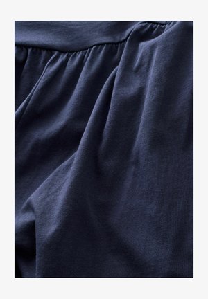 Námornícka modrá látka s mäkkou, hladkou textúrou. Obsahuje zhromaždené detaily na vrchu, ktoré vytvárajú skládané záhyby v materiáli.