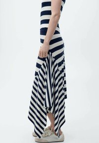 Gestreepte midi-jurk met marineblauwe en witte horizontale strepen, geribbelde bovenkant, uitlopende zoom en zachte stof, gecombineerd met beige sneakers.