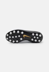 Suola nera di scarpini da calcio con tacchetti bianchi circolari, motivo di presa testurizzato e logo Nike dorato su una superficie liscia.