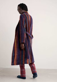 Gestreepte, pluche badjas in paars, rood en oranje met een strikceintuur. Draagt over geruite pyjamabroeken. Zachte textuur, relaxte pasvorm, middellange stijl.