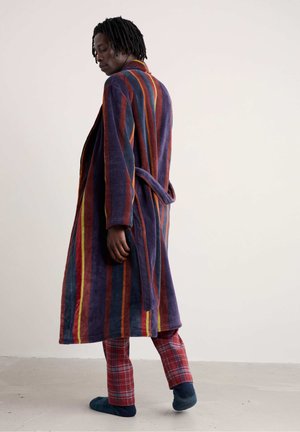 Svītrains, mīksts vannas apmetnis purpura, sarkanā un oranžā krāsā ar jostu. Valkāts virs bārdainās pidžamu biksēm. Mīksta tekstūra, brīvs piegriezums, vidēja garuma dizains.