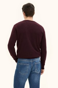 Burgunderfarbener Strickpullover mit Rundhalsausschnitt, langen Ärmeln und gerippten Bündchen, kombiniert mit blauen Jeans aus Denim mit zwei Gesäßtaschen.