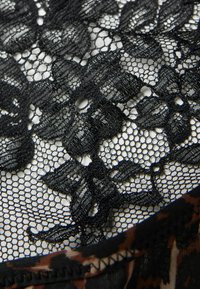 Czarna koronkowa tkanina z florystycznym wzorem i siateczkowym designem. Krawędź ozdobiona kontrastującym brązowym nadrukiem zwierzęcym.