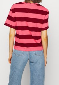 Short-sleeve t-shirt in pink and maroon stripes, cotton material, relaxed fit, with a round neckline and stitching detail at the hem.