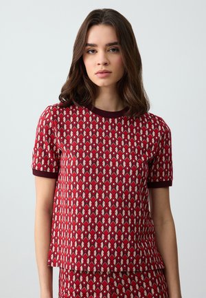 Red patterned short-sleeve top featuring a diamond design with cream and navy accents, finished with a dark ribbed crew neckline.