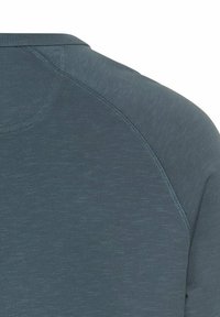 Granatowa koszula z fakturowanej tkaniny, z okrągłym dekoltem i rękawami raglanowymi, podkreślająca kontrastowe szwy wzdłuż szwów.