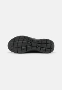 Semelle de chaussure en caoutchouc noir présentant un motif de grip texturé, avec une série de rainures rectangulaires et triangulaires pour l'adhérence et la stabilité.