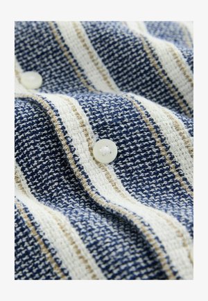 Audinių išpintų medvilnės su tamsiai mėlynomis, baltomis ir smėlio spalvos juostelėmis; į audinį yra įsiūta apvali balta mygtukas. Tekstūruota paviršius.