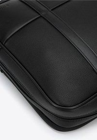 Sort læder laptoptaske med en struktureret finish, der har et glat toppanel og dobbelte lodrette accentstriber langs siderne. Lynlås-lukning.