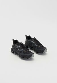 Schwarze Sportschuhe mit einem strukturierten Mesh-Obermaterial, ausgestattet mit einer dicken Sohle, Schnürverschluss und dezenten grauen Akzenten.