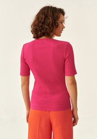 Top a manica corta aderente in tessuto a costine rosa con scollo rotondo, abbinato a pantaloni arancioni a gamba larga, visto da dietro.
