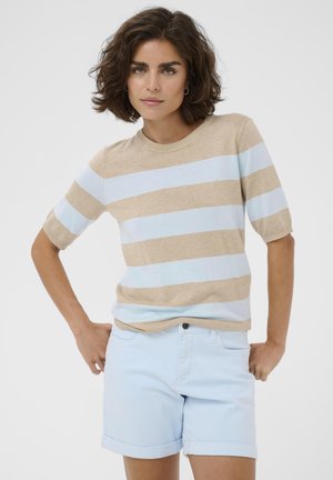 Kvinde med kort mørkt hår iført en kortærmet sweater med bordeaux og lyseblå striber og lyse denimshorts med opsmøgede kanter, hænderne på hofterne.