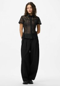Chemise noire transparente à boutons avec des manches courtes, ourlet arrondi et col pointu, associée à un pantalon noir ample à taille haute.
