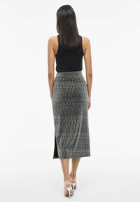 Haut sans manches noir associé à une jupe métallique noir et argent rayée, longueur genoux, avec une fente sur le côté et une texture douce.