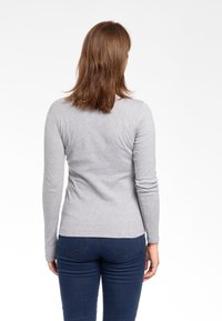 Maglietta grigia a maniche lunghe realizzata in tessuto morbido, design aderente con un leggero elastico, abbinata a jeans blu scuro, vista da dietro.