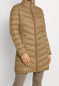 Brun pufferjacka med hög krage, vertikala sömmar och sidofickor, med dragkedjestängning och ett strukturerat tygmönster.