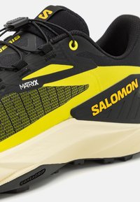 Baskets de course noires et jaunes avec un dessus texturé, des sections en maille et une semelle contournée portant la marque "Contagrip" en dessous.