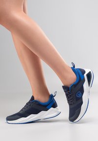 Granatowe buty sportowe z siateczkową tkaniną, białą podeszwą i niebieskimi akcentami. Charakteryzują się fakturowaną powierzchnią oraz sznurowanym fasonem z pętelką przy pięcie.