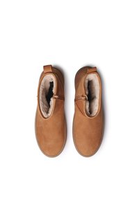 Bottines en daim marron avec une doublure douce en fausse fourrure, dotées d'une fermeture éclair sur le côté, d'une semelle plate et d'un design minimal. Aucun motif ni accent visible.