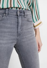 Los jeans de mezclilla grises presentan un diseño ajustado con una cintura de altura media, estilización de cinco bolsillos y detalles de costura sutiles.